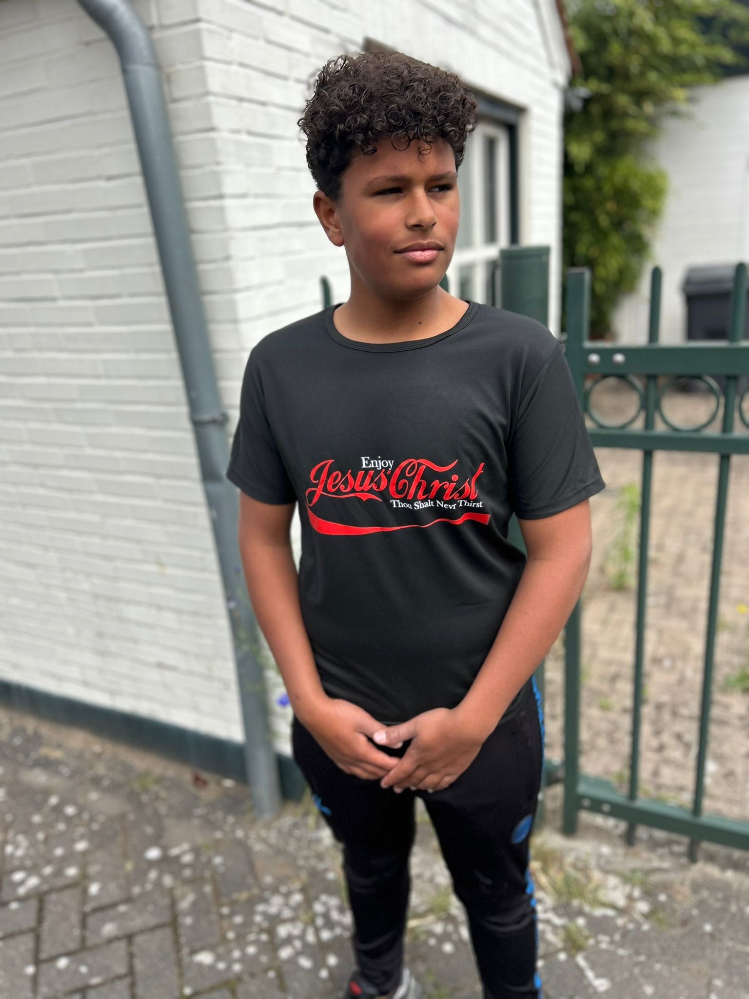 Jongen in een stijlvolle Jesus Is King T-Shirt van Onlyheknows2025, met opvallende rode opdruk op een diepzwarte achtergrond, perfect voor modebewuste jongeren die hun geloof uitdragen.