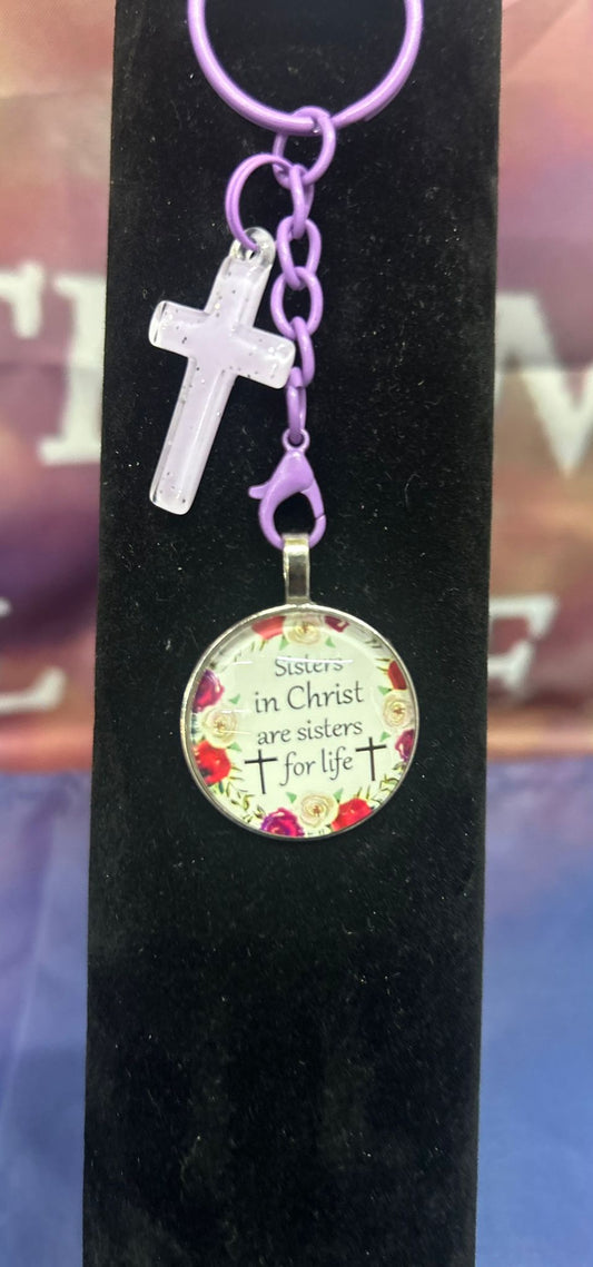 Stijlvolle Sleutelhanger 'Sisters In Christ' van Onlyheknows2025, met een elegante kruis en een ronde schijf met de tekst ‘Sisters in Christ are sisters for life’, symboliseert vriendschap en geloof.