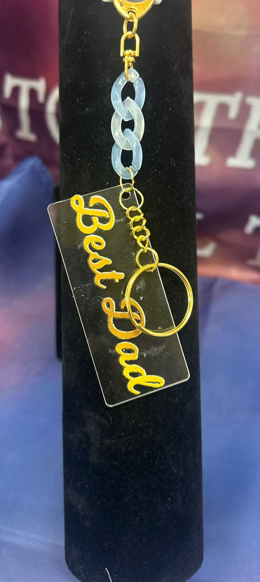 Sleutelhanger met gouden tekst 'Best Dad' op transparant acryl, met blauwe schakelkettinkje, ideaal als cadeau voor Vaderdag