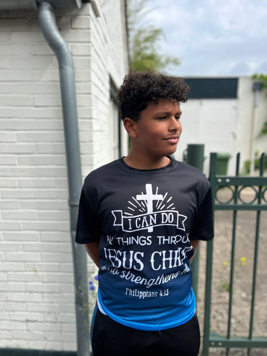 Christus T-Shirt van Onlyheknows2025, zwart katoen met krachtige witte en blauwe print, model poseert voor een muur en toont de inspirerende boodschap 'I can do all things through Jesus Christ who strengthens me'.
